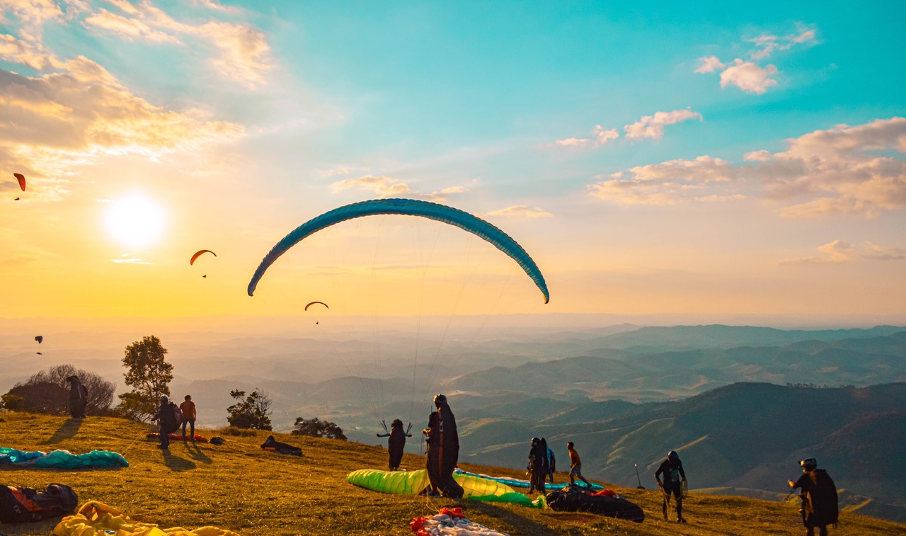 Essa imagem retrata varios atletas praticando voo livre nos ceus de Raul Soares