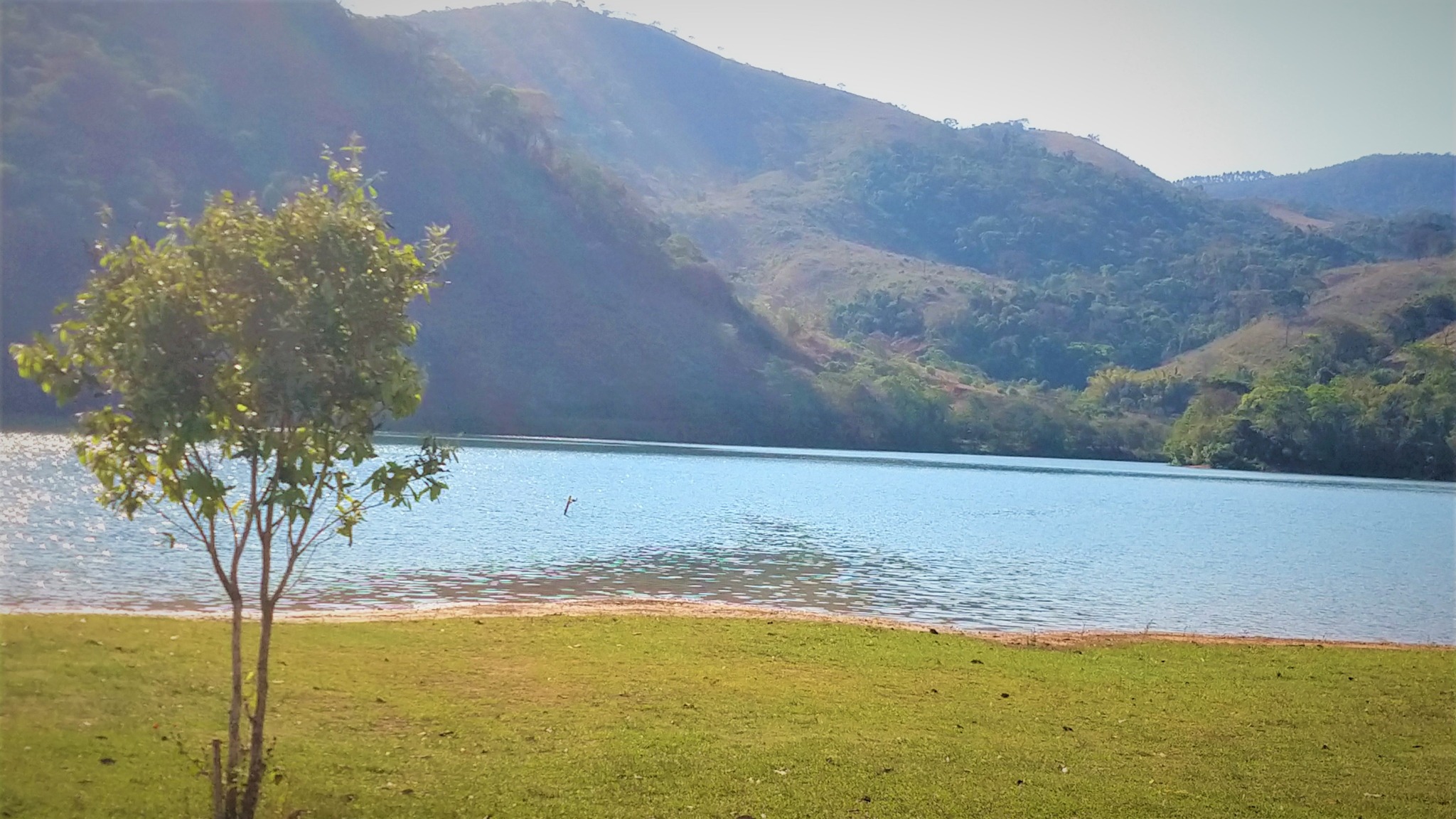Essa imagem retrata a represa do emboque, uma vista cênica de um reservatório azul calmo cercado por colinas verdes sob um céu claro